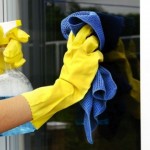 woman polishing glass door using microfiber cloth and yellow latex gloves